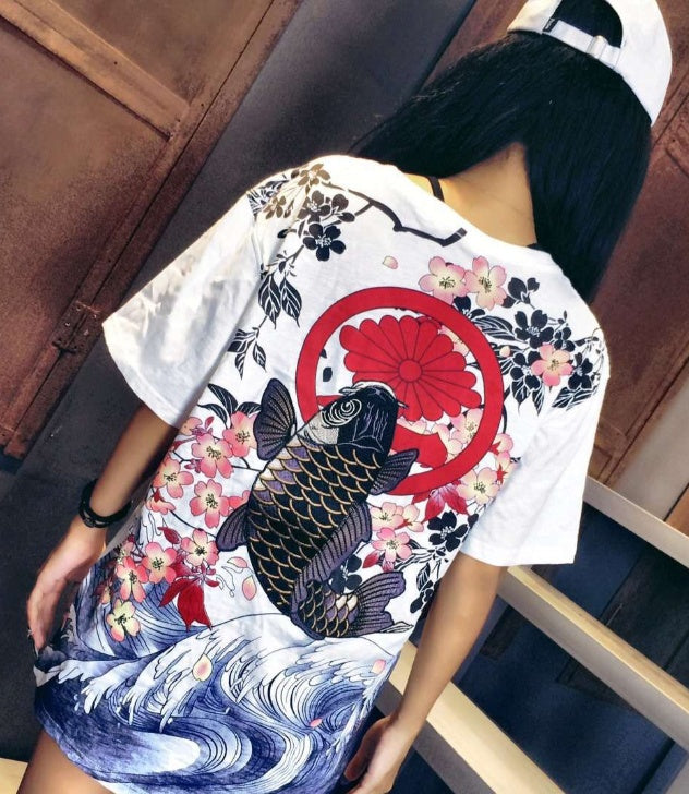 Person wearing a white t-shirt with a colorful design of a fish, flowers, and a red circle.